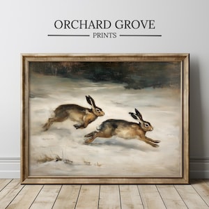 Puede incluir: Impresión enmarcada que representa dos liebres corriendo por un paisaje nevado. La obra de arte tiene una estética vintage con un marco de madera. El texto "ORCHARD GROVE PRINTS" se muestra en la parte superior.