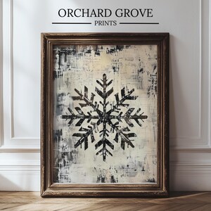Puede incluir: Impresión enmarcada con un diseño de copo de nieve negro sobre un fondo texturizado crema y gris. La obra de arte está encerrada en un marco de madera marrón oscuro. El texto "ORCHARD GROVE PRINTS" se muestra en la parte superior.