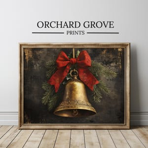 May include: A framed wall art print titled ORCHARD GROVE PRINTS featuring a golden bell adorned with a large red ribbon and green pine branches against a dark, textured background. The bell has an ornate decorative band near the bottom rim.