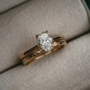 Puede incluir: Un anillo de compromiso de oro con un diamante de forma ovalada en una caja de anillo negra.