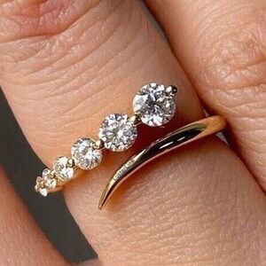 May include: A gold ring with a curved band and a row of small diamonds. The ring has a larger diamond set at an angle on the band.