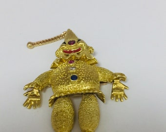 May include: A gold-toned, textured, clown figurine pendant with red, blue, and white gemstones. The pendant has a chain attached to the top.