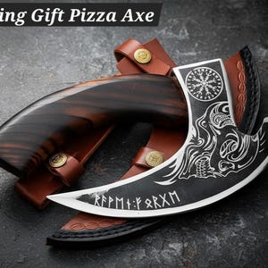May include: A Viking Gift Pizza Axe with a curved blade and a wooden handle. The axe features a black blade with white etched designs and runes. It rests in a brown leather sheath with gold-colored rivets. The text "Viking Gift Pizza Axe" is at the top.