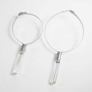 May include: A pair of silver hoop earrings with clear crystal drop pendants. The hoops are simple and circular, while the pendants are long and rectangular.