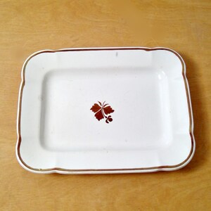 May include: White rectangular serving dish with a gold rim and a brown leaf design in the center.