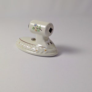 May include: White ceramic toilet paper holder shaped like an iron with a floral design.