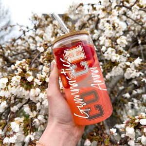 May include: A clear glass tumbler with a bamboo lid and a straw. The tumbler is filled with a pink liquid and has strawberries inside. The tumbler has white lettering that says "Go Cubs Go" and "Summer Vibes".