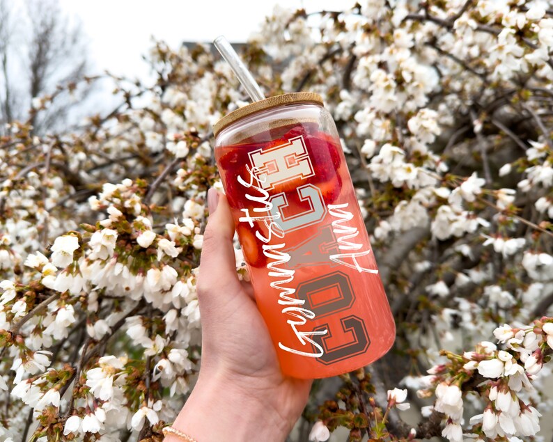 May include: A clear glass tumbler with a bamboo lid and a straw. The tumbler is filled with a pink liquid and has strawberries inside. The tumbler has white lettering that says "Go Cubs Go" and "Summer Vibes".