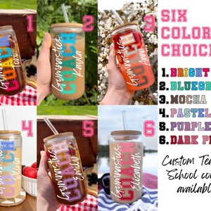 May include: Six different color options for a personalized tumbler with a gymnastics theme. The tumbler is clear glass with a bamboo lid and straw. The text on the tumbler says "Gymnastics" and includes a name. The text "SIX COLOR CHOICES" is displayed in pink letters with a black outline. The color options are listed below the text: 1. BRIGHT, 2. BLUEGREEN, 3. MOCHA, 4. PASTEL, 5. PURPLE, 6. DARK PINK. The text "Custom Team or School colors available." is displayed below the color options.