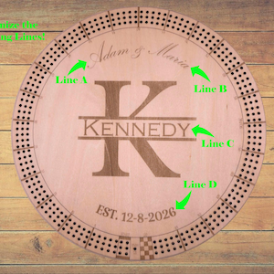 May include: A round wooden cribbage board with engraved details. The board features the name "KENNEDY" and the date "EST. 12-8-2026". It has a circular track with numerous holes for pegs and the names "Adam & Maria" are also engraved.