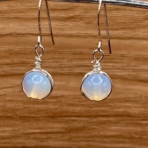 May include: A pair of silver earrings with white opal stones. The earrings are simple and elegant, perfect for everyday wear.