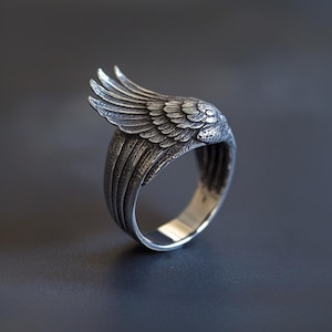 Puede incluir: Un anillo de plata con un diseño de ala detallado. El ala es texturizada y tiene un aspecto realista.