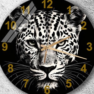 May include: Black and white clock with a leopard face design. The clock face has gold numbers and hands.