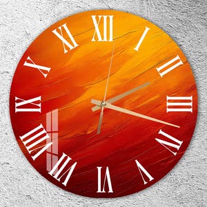Puede incluir: Reloj de pared redondo con un diseño abstracto en tonos rojos, naranjas y amarillos. La esfera del reloj presenta números romanos blancos y manecillas doradas. El reloj está montado en una pared texturizada gris claro.