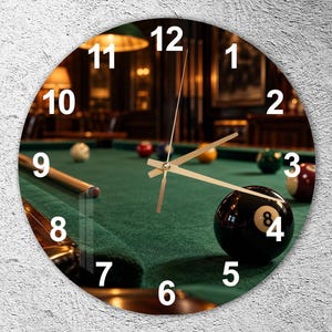 May include: A circular wall clock featuring a high-resolution print of a green felt pool table with scattered billiard balls and a cue stick. The clock face displays white numbers from 1 to 12 and includes thin gold-colored hour, minute, and second hands.