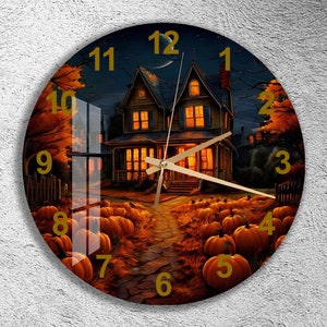 May include: A round clock with a Halloween theme. The clock face features a spooky house with lit windows, pumpkins, and a winding path. The numbers on the clock face are in gold and the hands are gold.