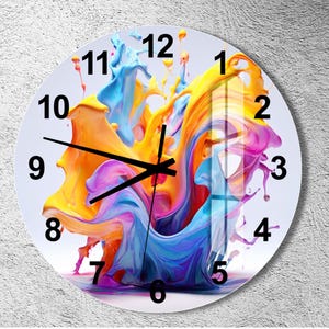 May include: A circular wall clock featuring a vibrant, abstract design of swirling yellow, blue, and magenta paint splashes. The clock face has a white background with bold black Arabic numerals from 1 to 12 and three thin black clock hands.