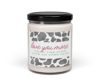 Może przedstawiać: Biała świeca w szklanym słoiku z czarną pokrywką. Etykieta zawiera wzór w krowie łaty i tekst "love you more than the cows love an open gate" w kolorze różowym i zielonym.