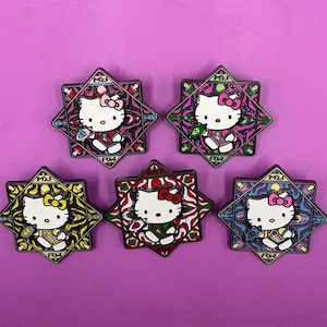 May include: Five Hello Kitty enamel pins. Each pin features Hello Kitty in a stained-glass style design, with a star-shaped border. The pins have different color schemes, including pink, red, yellow, and blue, with the letters "RW" visible.