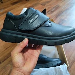 May include: Black leather shoes with a velcro strap and the word "FitVille" on the strap. The shoes have a white sole.