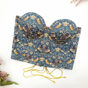 May include: A strapless corset top with a blue and white floral print featuring birds. The corset has a yellow lace-up back.