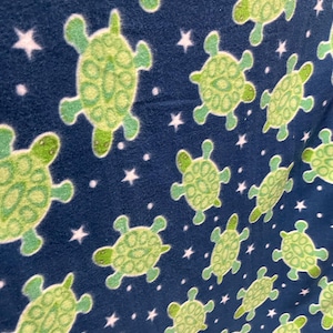 May include: A navy blue fabric with a repeating pattern of green turtles and white stars. The turtles have a detailed shell design and are outlined in a darker green. The stars are small and scattered across the fabric.