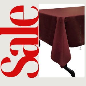 May include: A burgundy rectangular tablecloth with a smooth, wrinkle-free finish. The tablecloth is draped over a table with black legs.
