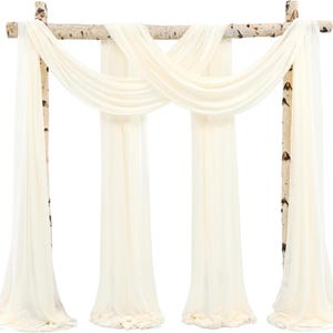Puede incluir: Un arco de boda color crema con tela drapeada. El arco está construido con ramas de abedul y presenta una tela transparente y fluida. La tela está dispuesta en un patrón entrecruzado en la parte superior y cuelga en paneles largos.