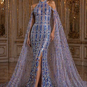May include: A lavender formal gown with a high neckline and a flowing cape. The dress is embellished with blue and silver details. The gown features a thigh-high slit and is decorated with sparkling sequins.