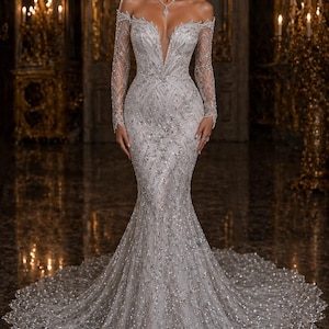 Peut inclure: Une robe de mariée argentée à épaules dénudées avec un décolleté plongeant et de longues manches transparentes. La robe est ornée de broderies de perles complexes et d'une jupe évasée. La couleur de la robe est un blanc argenté doux, créant un look glamour et élégant.