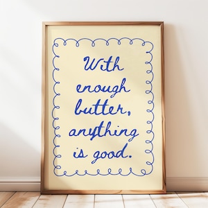 May include: A framed print with a yellow background and a blue cursive quote that reads "With enough butter, anything is good." The quote is surrounded by a blue decorative border.