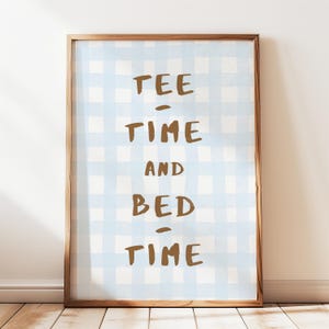 May include: A framed print with the words "TEE - TIME AND BED - TIME" in brown letters. The background is a light blue and white checkered pattern. The frame is a light brown color.
