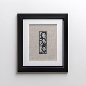 Könnte beinhalten: Schwarz gerahmtes Kunstwerk mit einem vertikalen Streifen aus vier Schwarz-Weiß-Porträts im Fotoautomatenstil. Die Fotos zeigen lächelnde und lachende Menschen. Das Kunstwerk ist auf einem neutralen Leinenhintergrund montiert.