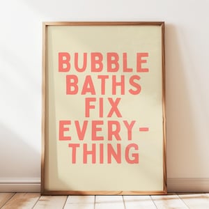 May include: A framed print with the text "BUBBLE BATHS FIX EVERYTHING" in coral-colored letters on a cream background. The wooden frame has a natural finish. The print is displayed against a white wall.