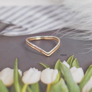May include: A gold and silver V-shaped ring on a gray surface with white tulips and the word "COCO" in the background.