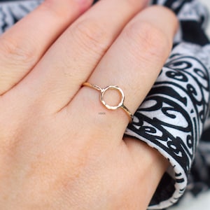 May include: A gold ring with a simple, open circle design. The ring is worn on a finger.