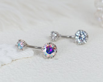 May include: A silver belly button ring with two clear iridescent stones. The larger stone is in the center and the smaller stone is on the top of the ring.