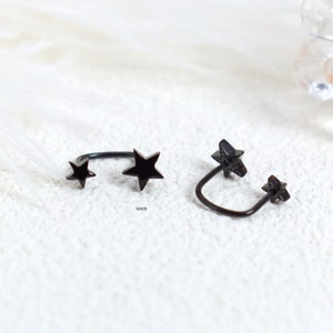 Puede incluir: Dos pendientes tipo ear cuff de metal negro, cada uno con dos dijes en forma de estrella unidos a una banda curva. Las estrellas var&iacute;an ligeramente en tama&ntilde;o, con una estrella m&aacute;s grande y una m&aacute;s peque&ntilde;a en cada pieza de acabado oscuro.
