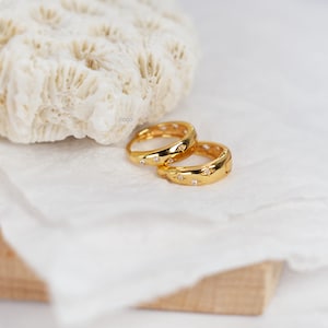 May include: A pair of gold hoop earrings featuring a polished finish and small, embedded star-shaped accents with clear stones. The earrings have a hinged closure mechanism and a rounded profile, showcasing a bright metallic yellow gold tone.