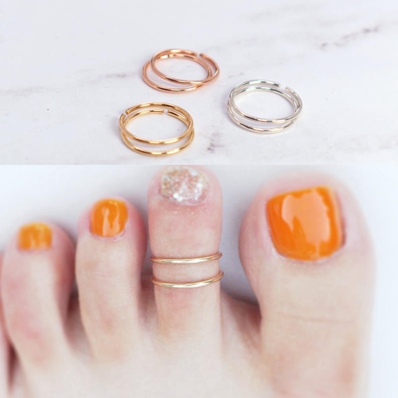 May include: Three thin, open-ended metal rings in rose gold, yellow gold, and silver tones. One gold ring is shown worn on a toe, featuring a double-band design. The rings are simple, circular, and metallic, with a smooth, polished finish throughout.