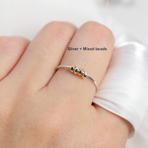 May include: A silver ring with mixed beads. The ring features a thin silver band with three small beads in gold and silver tones. The text "Silver + Mixed beads" is visible.