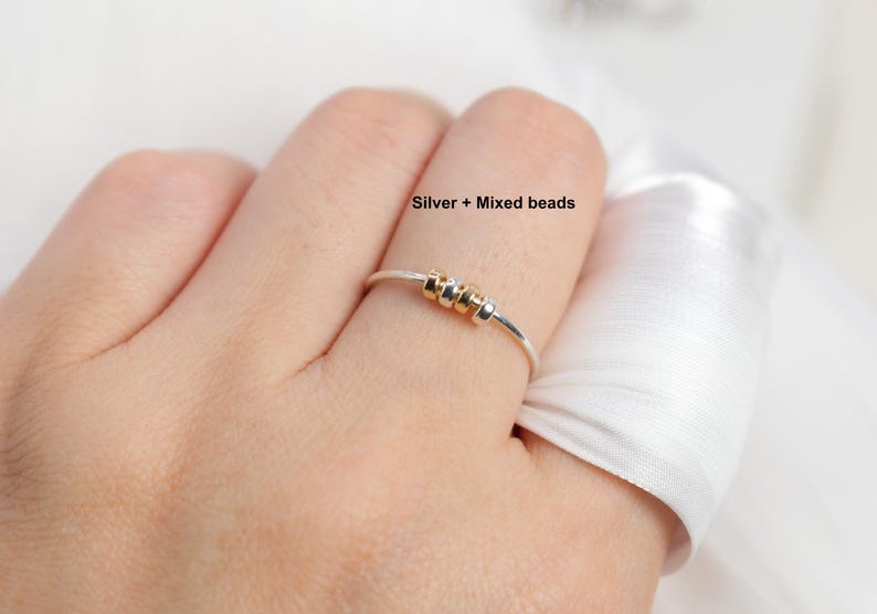 May include: A silver ring with mixed beads. The ring features a thin silver band with three small beads in gold and silver tones. The text "Silver + Mixed beads" is visible.