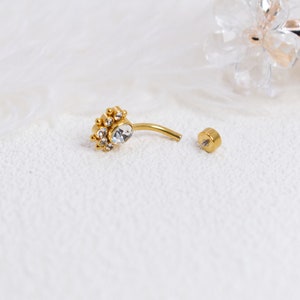 May include: Gold belly button ring with a clear crystal center and smaller crystals around it. The ring is separated into two pieces, the top piece with the crystals and the bottom piece with a small ball.