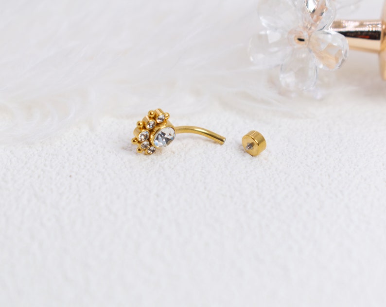 May include: Gold belly button ring with a clear crystal center and smaller crystals around it. The ring is separated into two pieces, the top piece with the crystals and the bottom piece with a small ball.