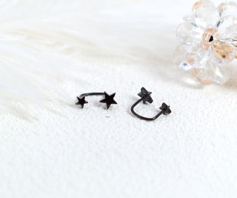 Puede incluir: Dos pendientes tipo ear cuff de metal negro, cada uno con dos dijes en forma de estrella unidos a una banda curva. Las estrellas var&iacute;an ligeramente en tama&ntilde;o, con una estrella m&aacute;s grande y una m&aacute;s peque&ntilde;a en cada pieza de acabado oscuro.
