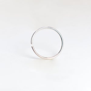 May include: A thin, circular silver-colored hoop ring with a small, visible gap in the metal band. The ring has a smooth, polished metallic finish and maintains a consistent, slender thickness throughout its entire circumference.