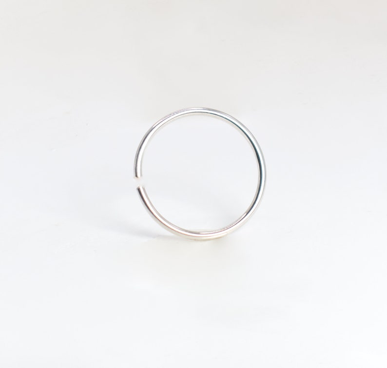 May include: A thin, circular silver-colored hoop ring with a small, visible gap in the metal band. The ring has a smooth, polished metallic finish and maintains a consistent, slender thickness throughout its entire circumference.