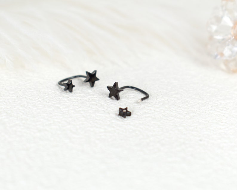 Puede incluir: Un conjunto de piezas de joyer&iacute;a de metal negro con dise&ntilde;os en forma de estrella. El set incluye dos pendientes o anillos abiertos y curvados con estrellas en los extremos, y una peque&ntilde;a pieza de pendiente tipo bot&oacute;n con forma de estrella.