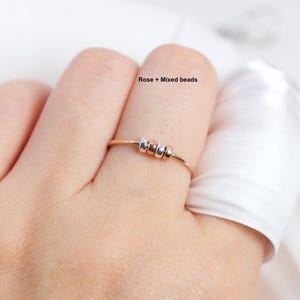 May include: A rose gold ring with three mixed beads. The ring is delicate and simple, featuring a thin band and small, colorful beads. The text "Rose + Mixed beads" is visible in the image.