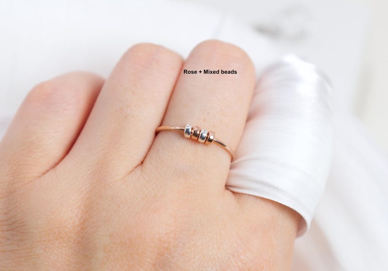May include: A rose gold ring with three mixed beads. The ring is delicate and simple, featuring a thin band and small, colorful beads. The text "Rose + Mixed beads" is visible in the image.